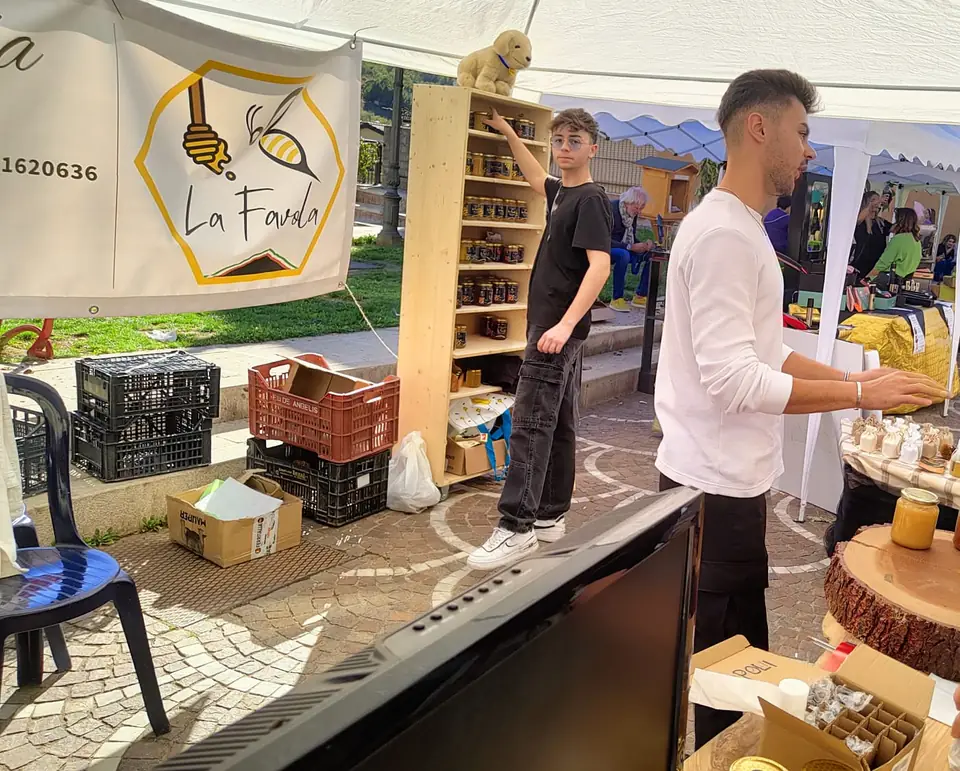 Il banco La Favola in piazza, con lo striscione e lo scaffale di legno pieno di vasetti