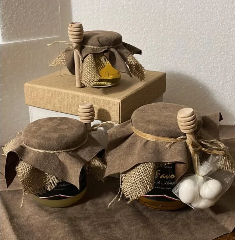 Vasetti di miele con cappellino in pelle scamosciata, juta, mestolino di legno e confetti, su una scatola regalo